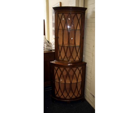 An Edwardian mahogany bow fronted floorstanding corner cabinet, the dentil and arcaded cornice over a pair of shaped barred g