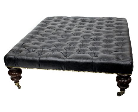 A LARGE BLACK LEATHER BUTTON UPHOLSTERED RECTANGULAR STOOL with four large turned mahogany feet terminating in brass casters,