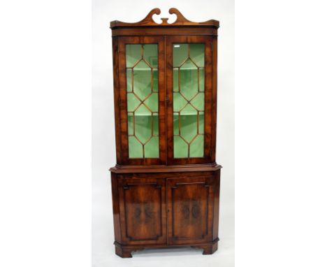 A REPRODUCTION YEW WOOD VENEERED CORNER CABINET with astral glazed doors above two panelled doors below and standing on brack