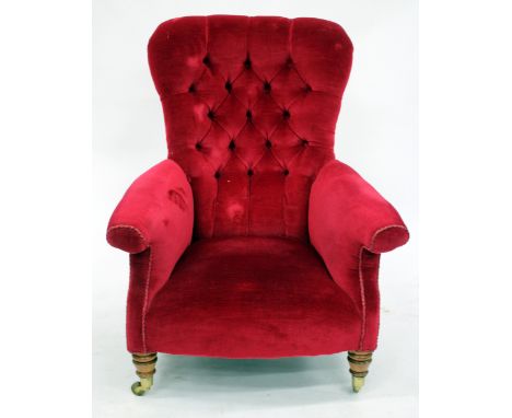 AN OLD RED DRAYLON BUTTON UPHOLSTERED ARMCHAIR with turned tapering front legs terminating in brass casters
