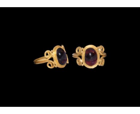 An undated archaistic gold ring in 1st century AD style comprising a bifidf hoop with scrolled ends supporting a discoid plaq