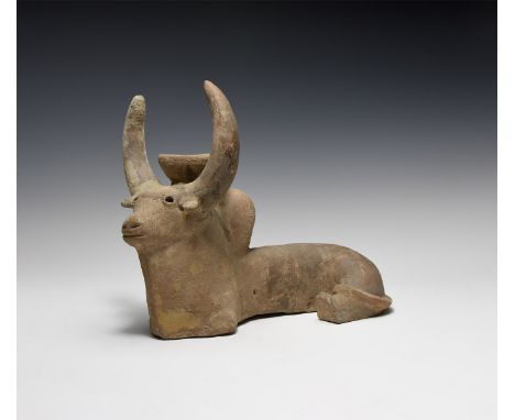 An undated archaistic hollow-formed ceramic zebu figurine in reclining pose with socket between the horns, painted detailing.