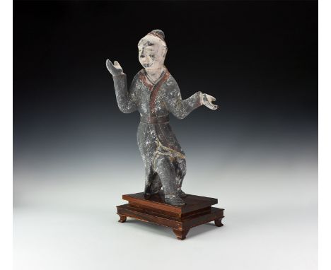 An undated archaistic ceramic figure of a dancer in active pose with hands spread, wearing a belted riding coat and trousers,