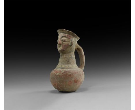 An undated archaistic ceramic ewer with bulbous body, tall tapering neck, stylised female head below the flared rim with stra