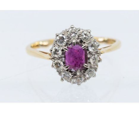 An 18ct gold and ruby cluster ring, comprising a central oval cut ruby, approx 5 x 6mm, within a border of round brilliant cu