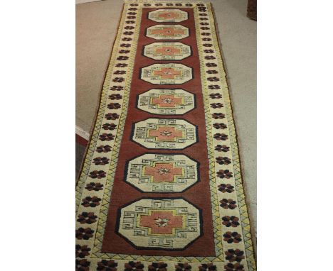A Turkish runner with repeating lozenge medallions within a flowerhead border. L.310 W.30cm. 
