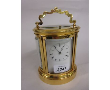 20th Century oval gilt brass carriage clock, the enamel dial with Roman numerals, the two train movement with hour repeat fun