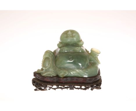 A CARVED JADE FIGURE OF A SEATED BUDDHA, modelled with a cup in his left hand, on a hardwood stand. 7.5cm by 13cm (exc. stand