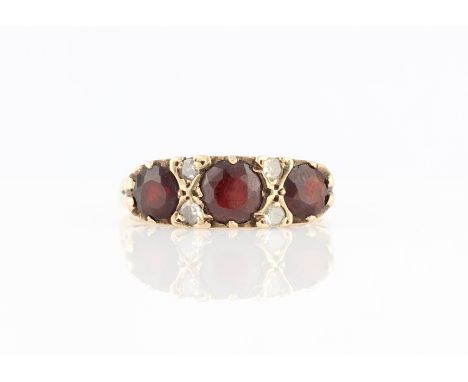 A hallmarked 9ct yellow gold garnet and diamond ring, set with three principal round cut garnets separated by eight-cut diamo