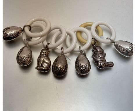 A collection of seven white metal chased child's rattles with composition teething rings, some in the form of Easter eggs, ca