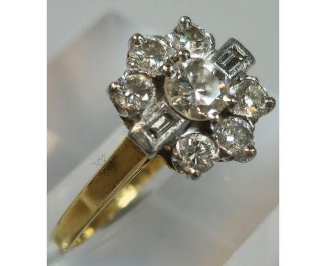 18ct gold and platinum diamond flowerhead ring, having seven brilliant round cut diamonds and two baguette cut diamonds. 3.2g