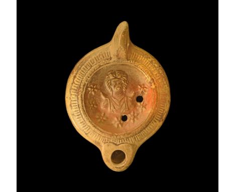 2nd century AD. A ceramic oil lamp with broad discoid body, stub nozzle with heart-shaped panel, pierced lug handle; the disc