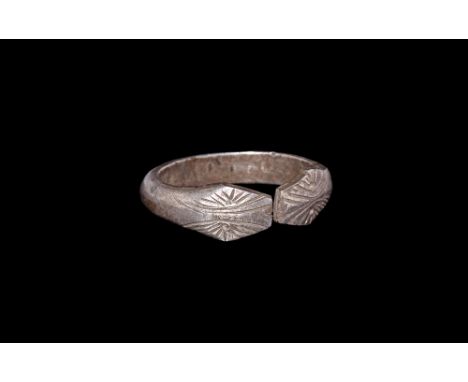 8th-9th century AD. A D-section silver penannular hoop with trapezoidal finials decorated as snake-heads with punched pellet 