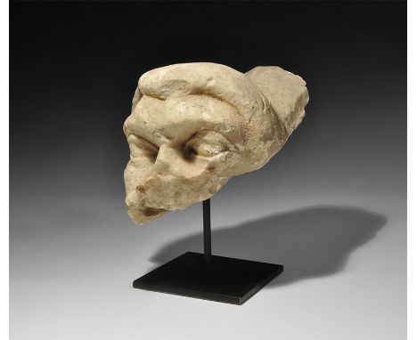 1st-3rd century AD. A fragment of a marble head of a young male, with headdress; the lentoid eyes carved deep-set with heavy 