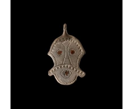 5th-6th century AD. A flat-section silver pendant with integral suspension loop, facing mask with long moustache extending be