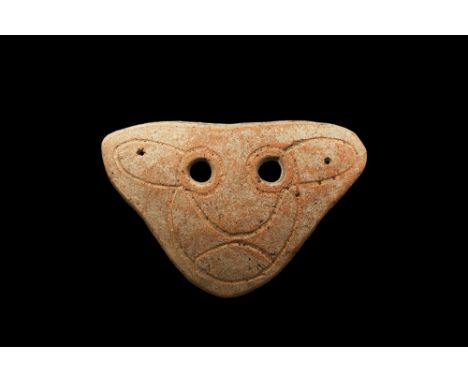 4th-3rd century BC. A triangular-shaped slightly curved ceramic mask with two eye-holes and incised stylised facial details; 