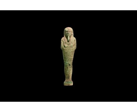 Late Period, 664-332 BC. An olive green glazed composition shabti with tripartite wig, false beard, tools in the crossed hand