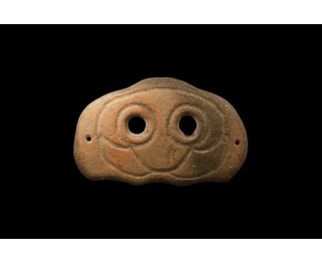 4th-3rd century BC. A rectangular-shaped slightly curved ceramic mask with two eye-holes and incised stylised facial details;