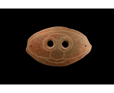 4th-3rd century BC. An oval-shaped slightly curved ceramic mask with two eye-holes and incised stylised facial details; pierc