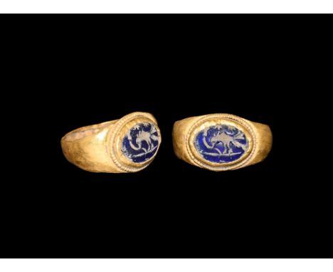 1st century AD. A D-section gold ring with expanding shoulders, discoid plaque with beaded wire collar, cell with blue glass 