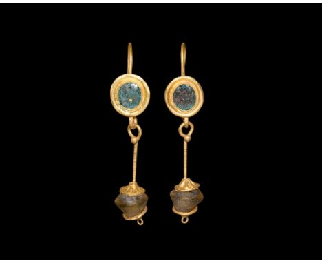 3rd century AD. A matched pair of gold earrings, each a discoid plaque with inset green glass cloison, dangle with twisted sh