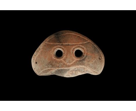 4th-3rd century BC. A D-shaped slightly curved ceramic mask with two eye-holes and incised stylised facial details; pierced a