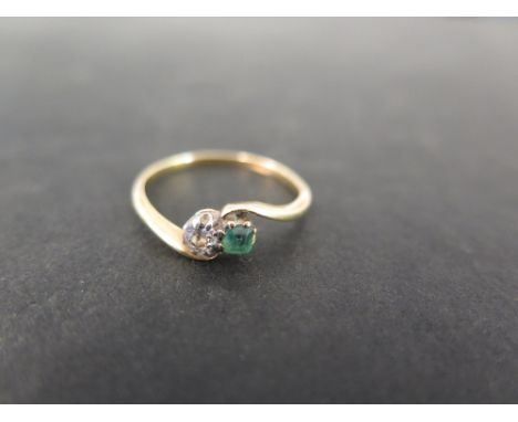 An emerald and diamond two-stone crossover ring - The old-cut diamond and cushion-cut emerald to the asymmetric shoulders and