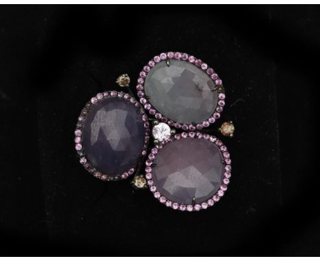 An 14 karat black rhodinated gold ring set with three large oval faceted pink sapphires, each framed with an entourage of sma