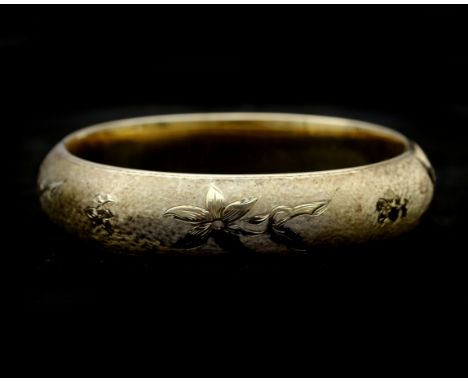 A 14 karat gold bangle with flower engraving. The bracelet has a satin frosting and is engraved with a floral motif. has a bo