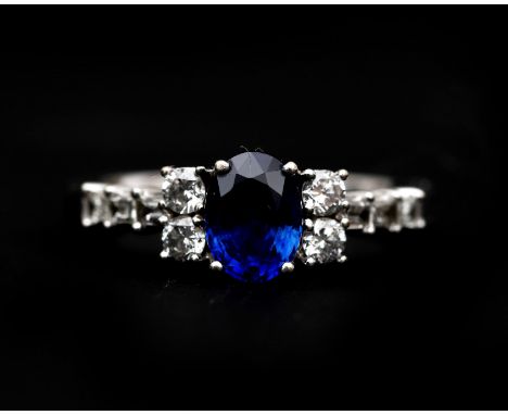 An 18 karat white gold ring set with an oval faceted blue sapphire approx. 0.70ct., four brilliant cut diamonds and six bague