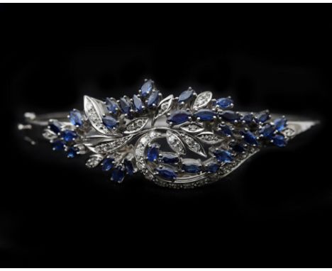 An 18 karat white gold bangle bracelet open worked with floral decoration, set with thirty-three navette cut sapphires, appro