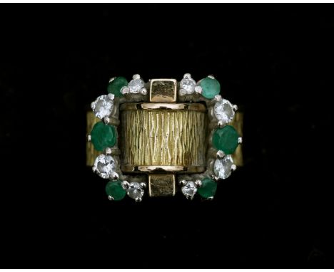 An 18 karat gold ring with diamonds and emeralds. The ring consists out of a ring band with wood pattern with a buckle like d