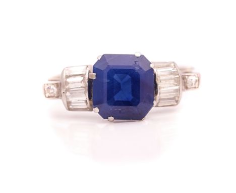 A SAPPHIRE AND DIAMOND RINGClaw set with the emerald cut sapphire to the centre, between baguette diamond set five stone ridg