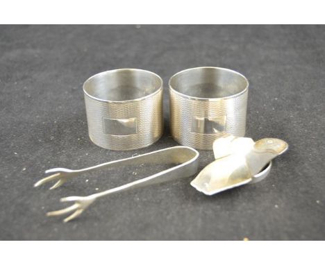 A pair of engine turned silver napkin rings, Birmingham 1943, a pair of silver sugar tongs of claw design, together with a si