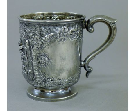 A silver Christening mug embossed with children playing on a gate. 9 cm high. 6.3 troy ounces.