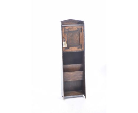 A 1920's oak bookcaseHaving a galleried top above a single cupboard door over a magazine rack and single shelf, 123cm high.