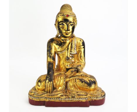 A carved hardwood, gilded and paste set model of Buddha, seated cross-legged wearing traditional robes, his left hand in Abha