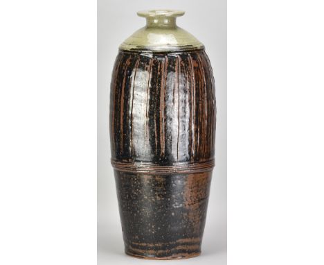 JIM MALONE (born 1946); a very tall part fluted stoneware bottle covered in tenmoku breaking to kaki glaze with green ash top