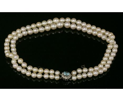 A two-row graduated cultured pearl necklace, c.1950,with a blue zircon and synthetic spinel cluster clasp.  Two rows of gradu