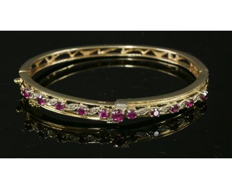 A 14ct gold, ruby and diamond crossover hinged bangle,with a row of graduated circular mixed cut rubies to the top half.  All