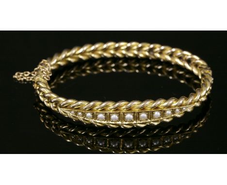 An Edwardian cased, split pearl gold bangle, c.1905,of oval hinged form.  The top section with an elongated boat-shaped centr