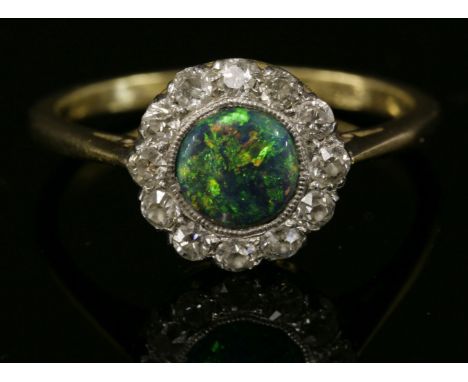 A black opal and diamond daisy cluster ring, c.1915,with a circular cabochon black opal, milligrain set to the centre, surrou