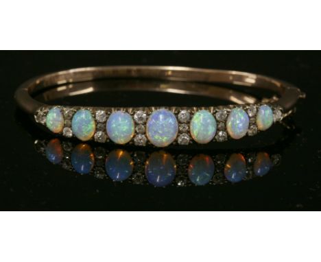 A late Victorian opal and diamond hinged bangle, c.1890,with a row of graduated oval cabochon opals, claw set to the top half