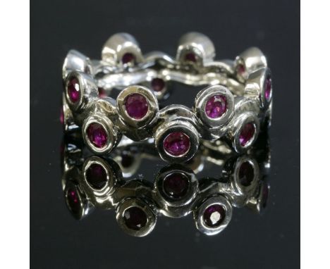 A Continental white gold ruby band ring,with a central wavy section.  A continuous row of circular mixed cut rubies, rub set 