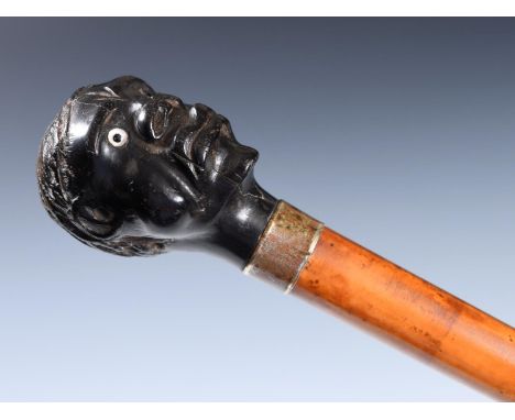 An early 20th century walking stick, with carved ebony handle, in the form of a man's head with glass eyes, with silver mount