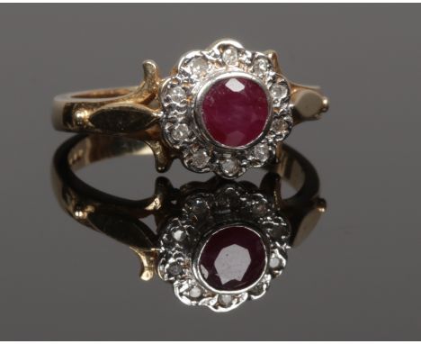 A 9ct gold ruby and diamond halo cluster ring set on scrolling shoulders, size M.