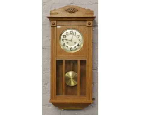 A carved light oak 8 day wall clock with silvered dial, pendulum and key.