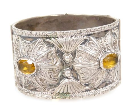 A Continental bangle, white metal, embossed in a floral and foliate design, set with four yellow stones, possibly citrines, w