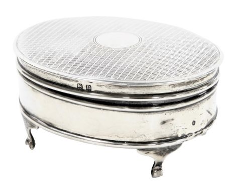 A George V silver oval dressing table box, with engine turned decoration, vacant circular reserve, raided on four scroll feet