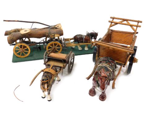 Three pottery cart horses, with wooden carts, one for tree trunk carrying, on a green rectangular base, the small 41cm long a